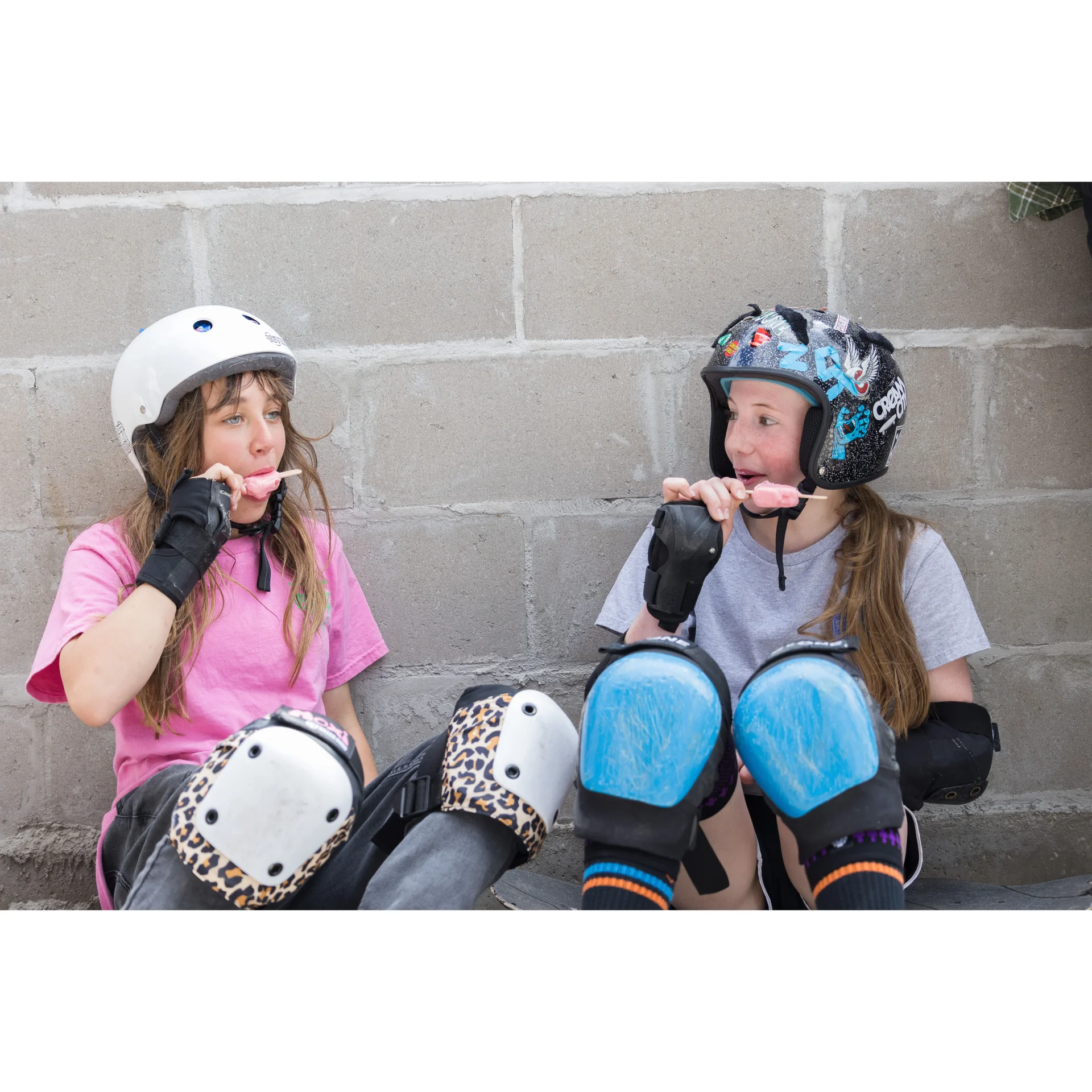 Couple of girl skaters all padded up enjoying a popsicle at a National DIY Skate Jam.